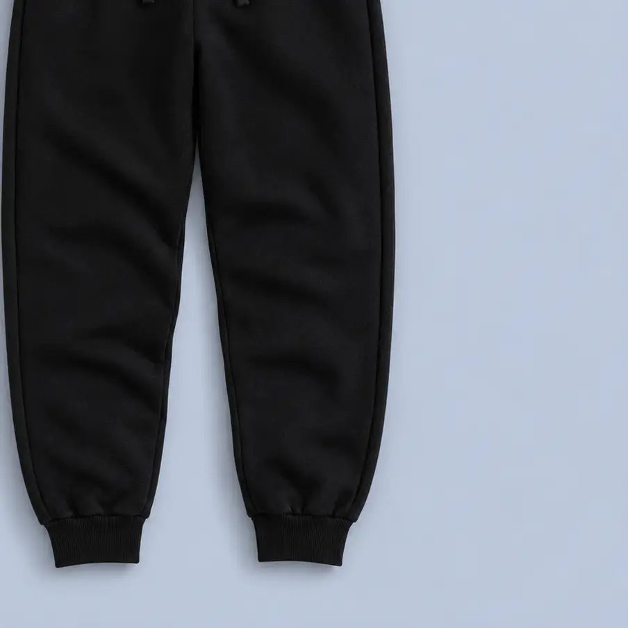 Pantalón de felpa negro con cordón y puño en el tobillo, doblado sobre fondo gris azulado
